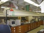 Chemistry Laboratory Fume Hoods Are Held High So Students Can See the Full Blackboard On Opposite Side of the Room.  Note White and Green Duct Pipes attached to top of hood box. The white pipe carries away the fumes while the green pipe delivers replacement air from outside the building. This reduces HVAC cost since the heated (or cooled) air from the room itself is not "sucked up" the hoods. The replacement air is delivered thru a screen full of holes just under where the sloping top portion of hood sticks out from the side of the hood.  Science Building,  USCA Campus, Aiken, SC.  ************************************  (Photo = 4986 ...... WayPt = `000 |w|' 420 ft)