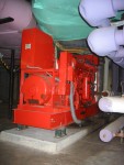 Another View of the Diesel Engine Co-Generator With Attached AC Power Generator.  Note coil spring supports under each corner of the Engine's Support Frame. These are vibration absorbing mounts to reduce the vibration of the engine from spreading to the entire building. Most items of machinery in this equipment room have similar vibration reduction supports. Rectangular Red Box above the AC Power Generator Houses Electrical Control Equipment for the generator.  HVAC Equipment Room, Basement of Science Building, USCA Campus, Aiken, SC.  ************************************  (Photo = 5137 ...... WayPt = `000 |w|' 420 ft)